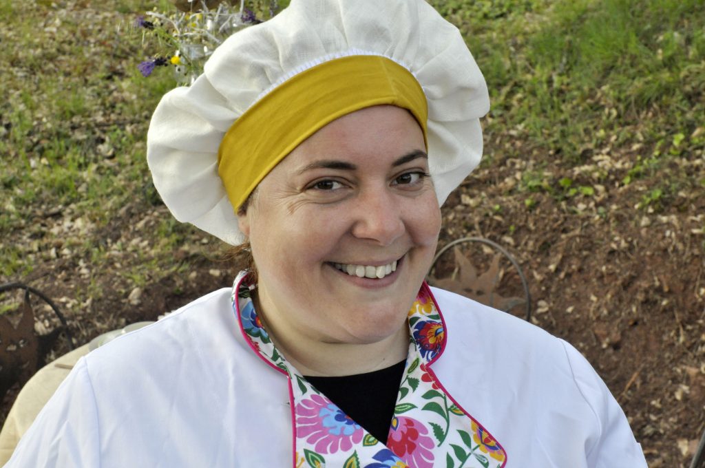 La cheffe Elodie Mendez en habit de cuisinière, veste blanche, col à motif fleuri, toque de chef.